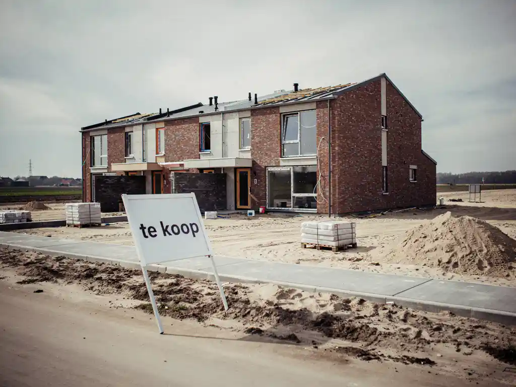 Halfafgebouwd nieuwbouwtussenwoning in Westland met een schuin staand te-koop-bord op een verlaten bouwterrein.