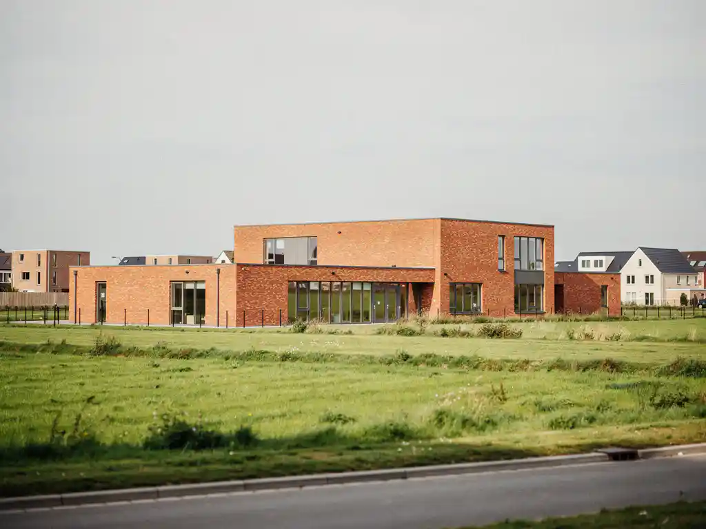 Nieuwe basisschool met rode bakstenen gevel in Midden-Delfland, omgeven door groene polderweiden en nieuwbouwwoningen.