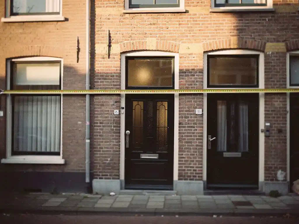 Smalle bakstenen gevel van een Haags rijtjeshuis in de Vruchtenbuurt, met meetlint van makelaar over de voorbreedte.